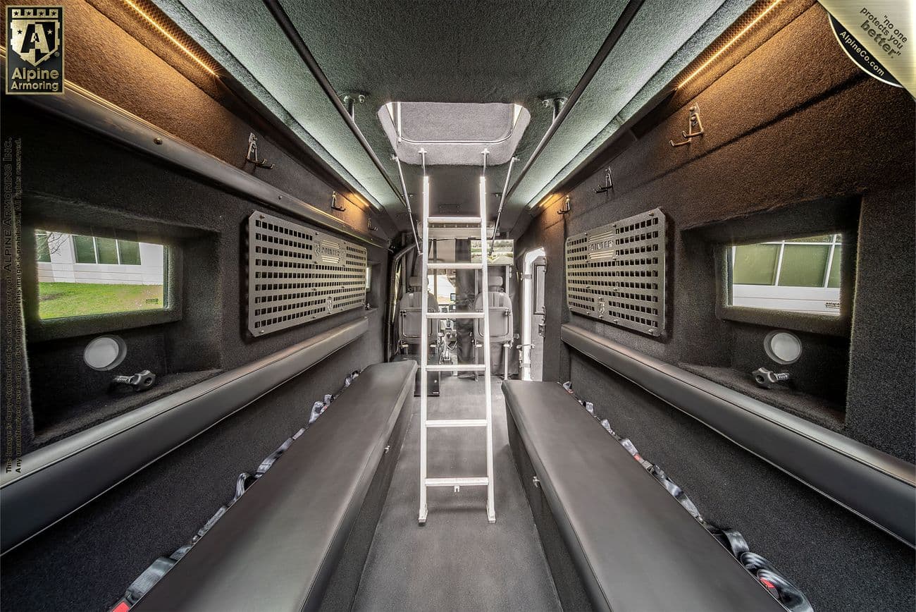 The interior of a black armored SWAT van, known as the Armored Pointer from Alpine Armoring, with the interior ladder set up showcasing reinforced windows, tactical lighting, and advanced security features. 